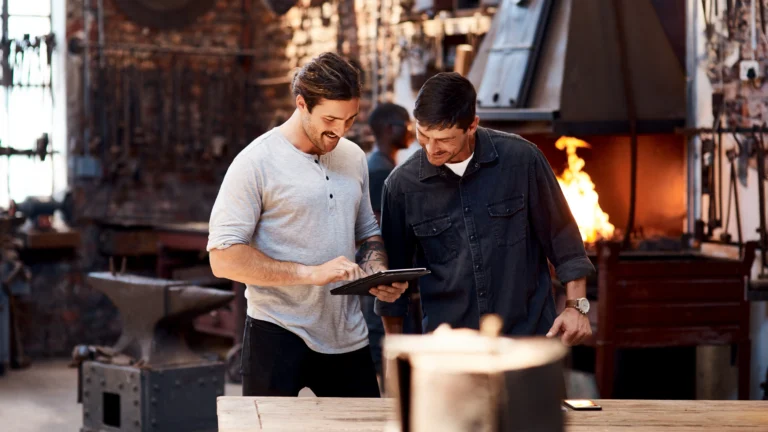 Two small business owners discussing technology solutions on a tablet in a workshop environment, showcasing small business technology adoption with Scorpion Five Technologies.