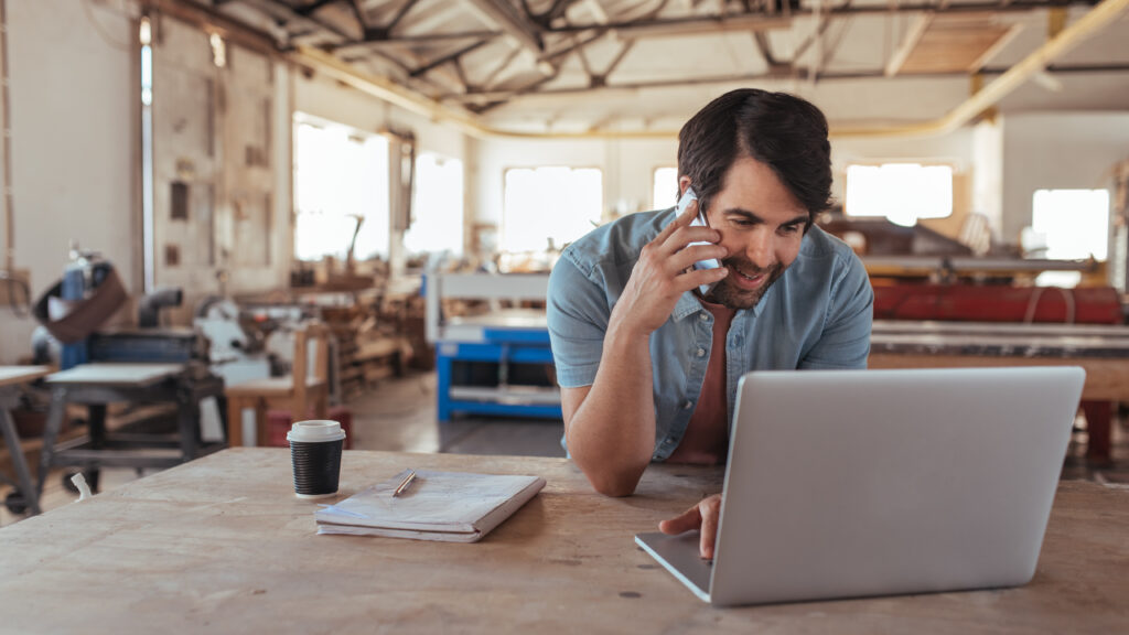 Small business owner using a laptop and phone to manage business operations, demonstrating how small business technology drives communication and growth with support from Scorpion Five Technologies.
