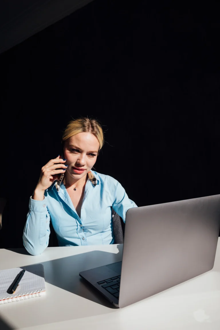 Entrepreneur using a laptop and phone to manage her growing business, reflecting the small business technology and digital marketing support offered by Scorpion Five Technologies.