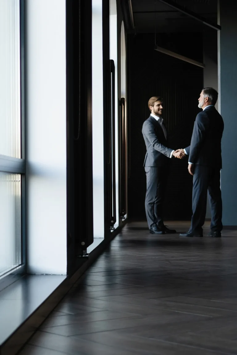 Two executives greeting each other in a modern office corridor—representing Scorpion Five Technologies' commitment to supporting large organizations and government agencies with enterprise systems, cloud engineering, and cybersecurity accreditation needs.