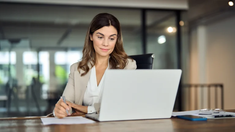 Confident female manager reviewing Agile software development lifecycle reports on laptop in modern office — representing Scorpion Five Technologies' (S5T) expertise in Agile development frameworks, iterative development, and SDLC project management for high-performance software teams.