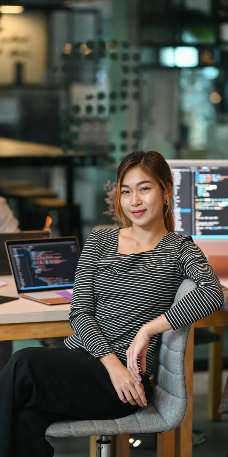 A young software engineer from Scorpion Five Technologies (S5T) sits in front of multiple monitors containing code along with other developers, demonstrating the collaborative nature of custom software development.