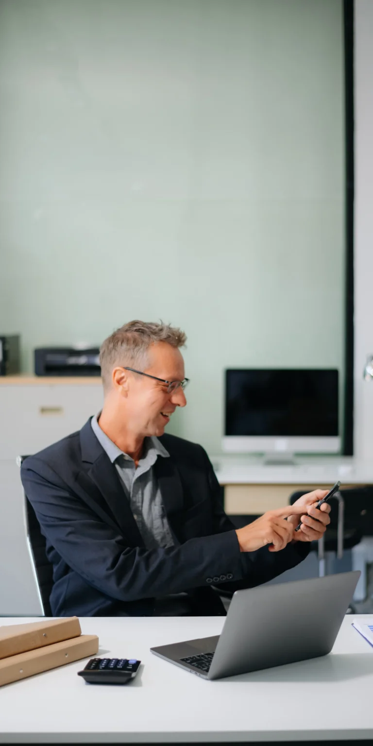 Professional using a smartphone and laptop in a modern office—representing how Scorpion Five Technologies empowers small businesses with mobile-ready digital marketing strategies to stay connected and competitive.