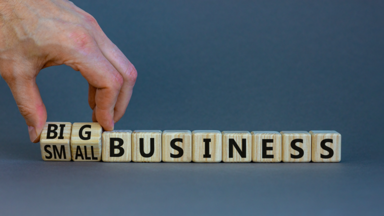 Wooden blocks spelling 'SMALL BUSINESS' with a hand changing 'SMALL' to 'BIG'—illustrating how custom software development strategies differ for small businesses versus large enterprises.