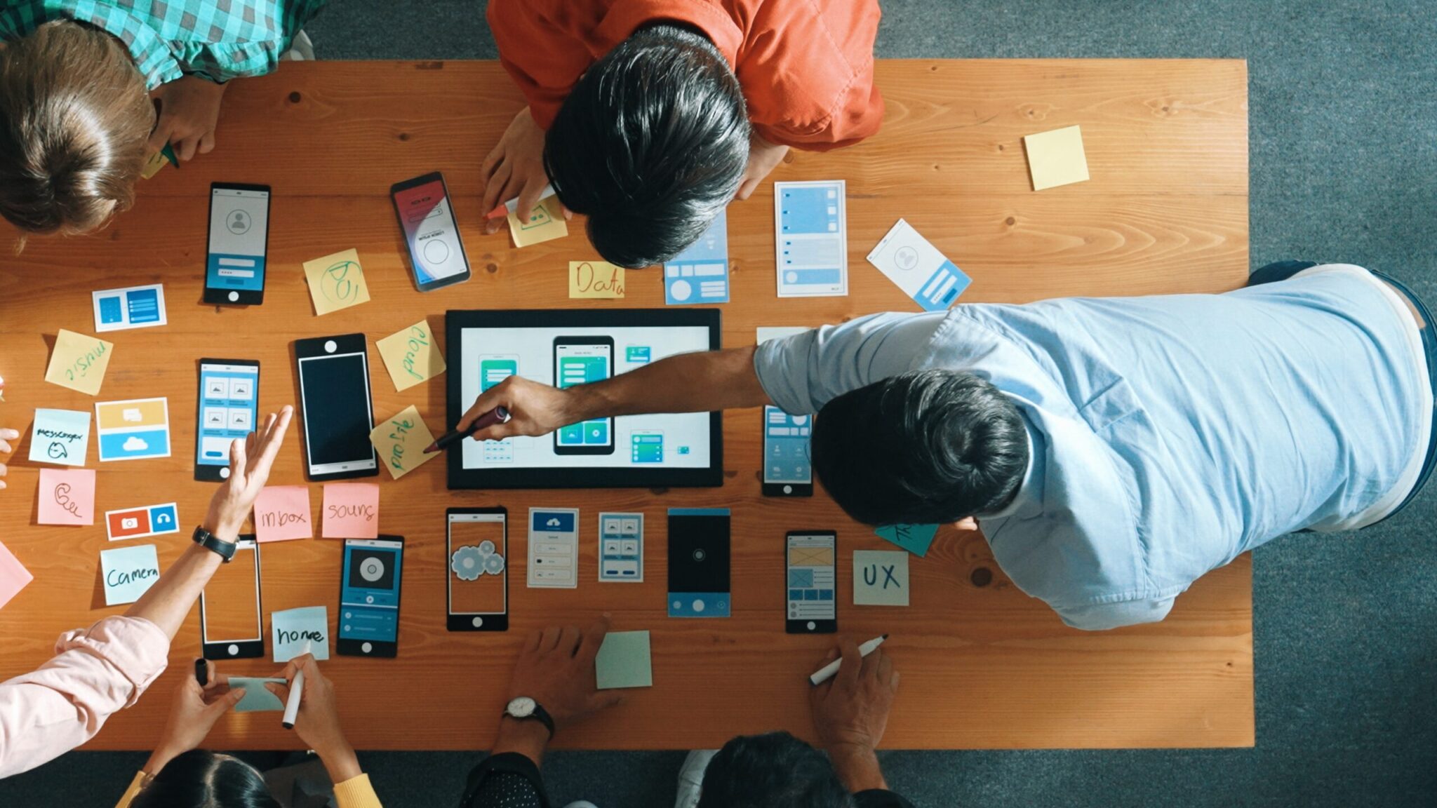 Team collaborating on mobile UI wireframes and prototypes during the design phase of custom software development—visualizing user experience and business workflows on paper and tablet.