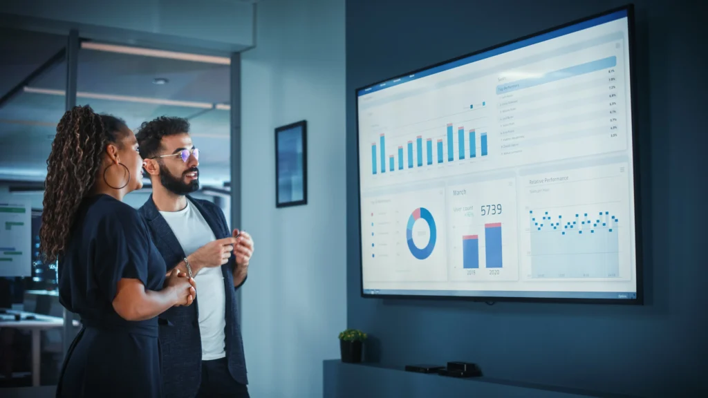 Two business professionals reviewing digital dashboards with charts and graphs, representing how small businesses measure key marketing metrics like traffic, engagement, and ROI.”