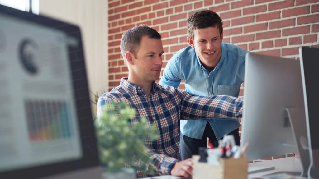 Two small business professionals collaborating on digital marketing strategy at a computer, reviewing charts and online performance data.